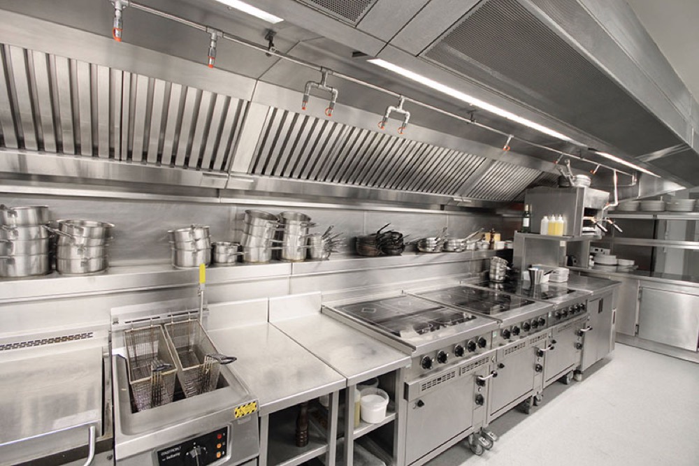 Stainless commercial kitchen with hood over cooking line